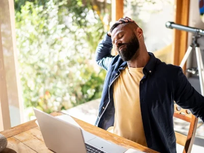 Homme travaillant dans son bureau à domicile et ressentant des douleurs corporelles dues à une position assise trop longue