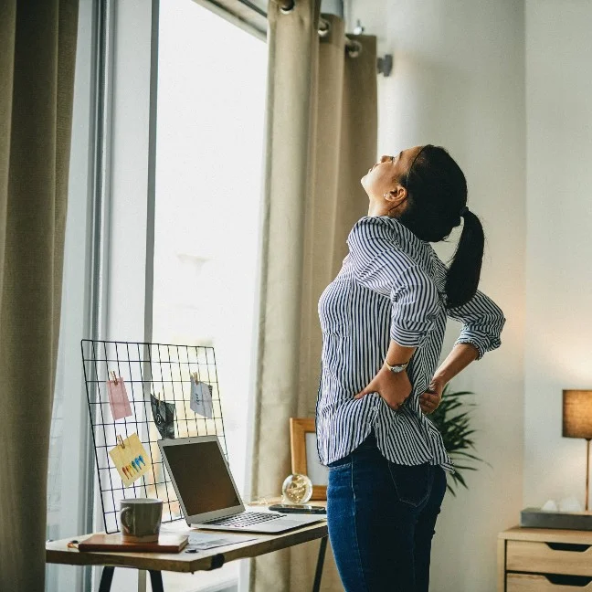 Femme s'étirant dans son bureau à domicile pour soulager les douleurs lombaires dues à une position assise prolongée