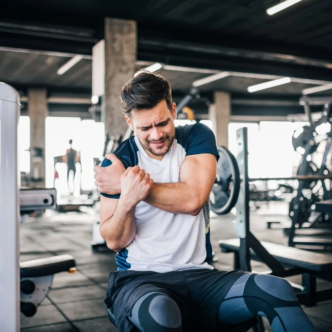 Un homme ressentant une douleur à l'épaule après avoir fait de l'exercice en soulevant des poids dans une salle de sport