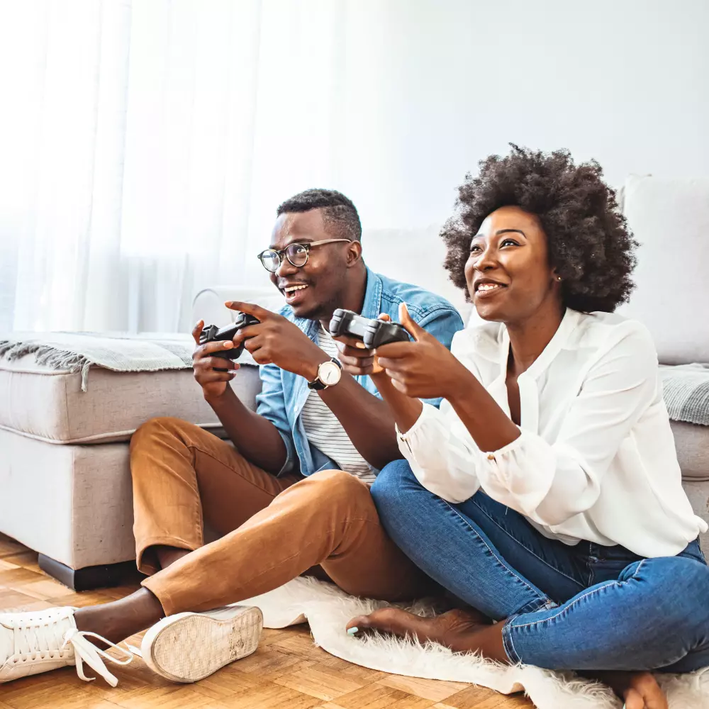 Un jeune couple jouant à des jeux vidéo, assis sur le sol de leur salon avec une mauvaise posture