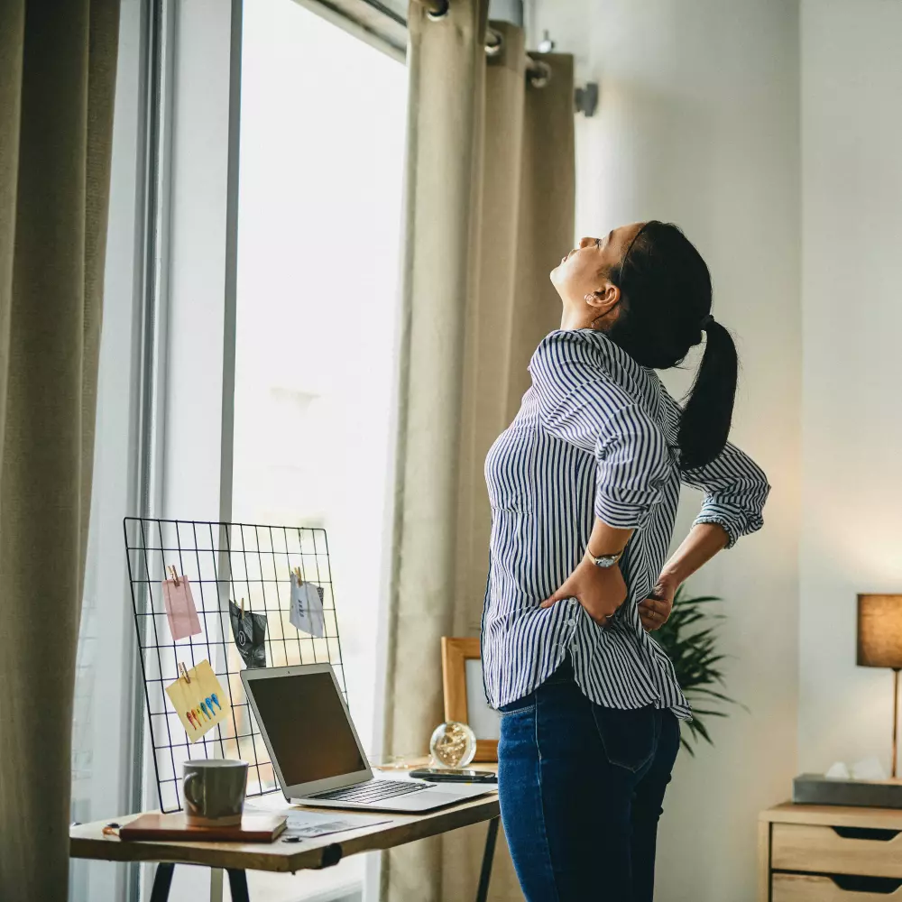 Femme s'étirant dans son bureau à domicile pour soulager les douleurs lombaires dues à une position assise prolongée